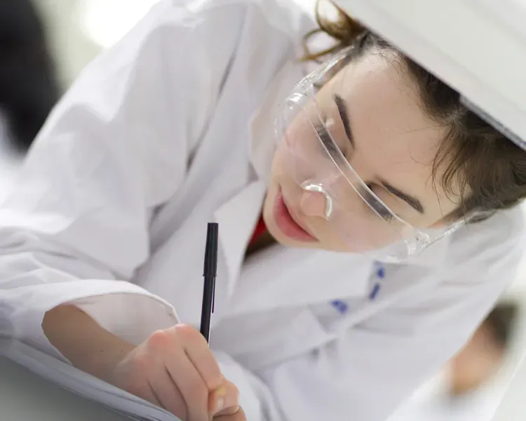 Student in white coat in lab at a machine