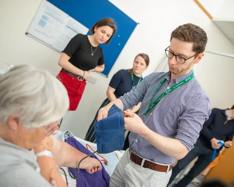 Medical student taking the blood pressure of a patient while others observe