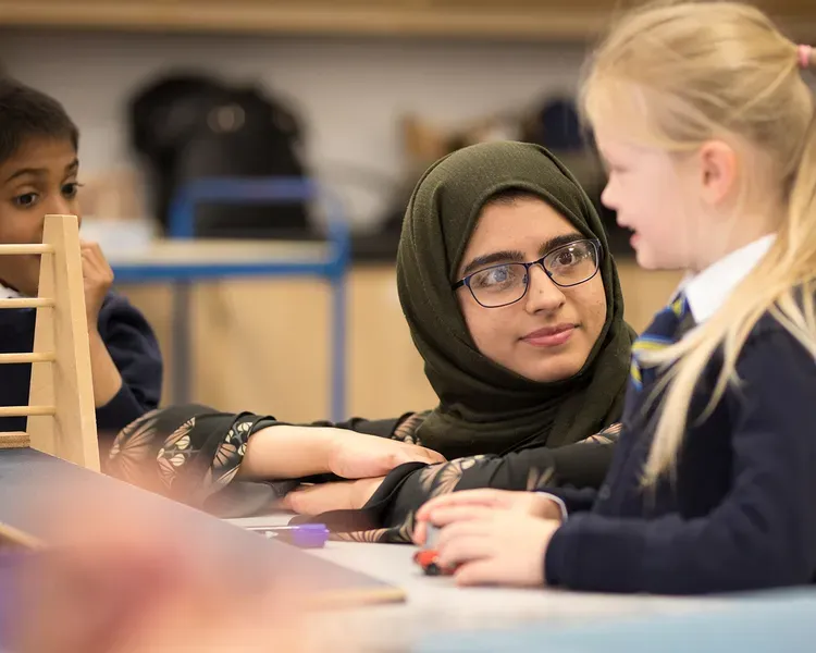 A teacher helping students use a model of a wooden ramp