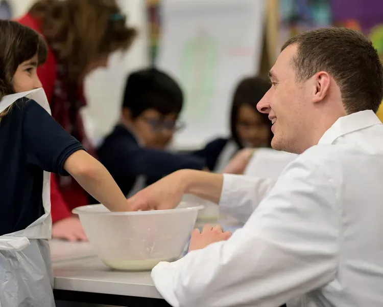 A teacher helping a girl mixing something in a bowl