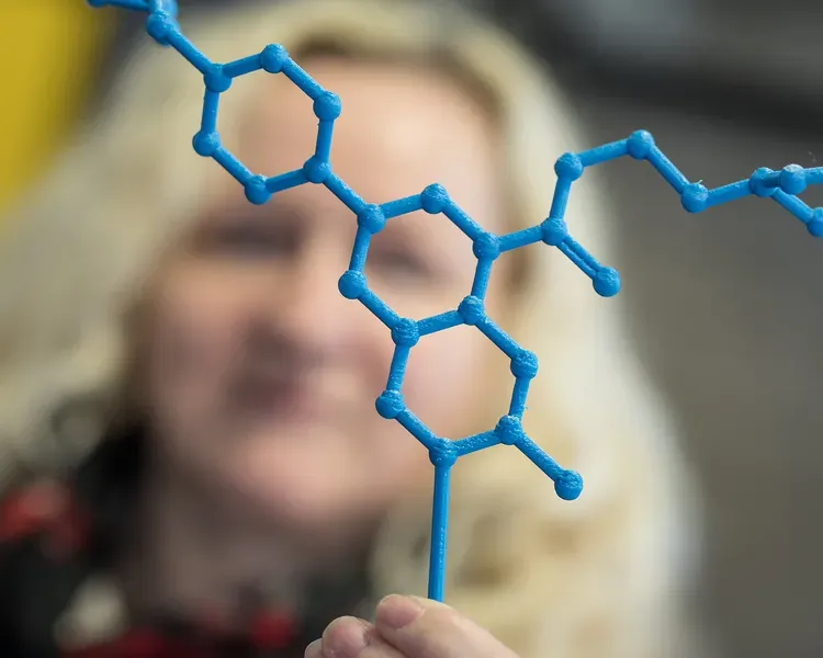 A woman, blurry, holding up a 3D printed molecule, in focus