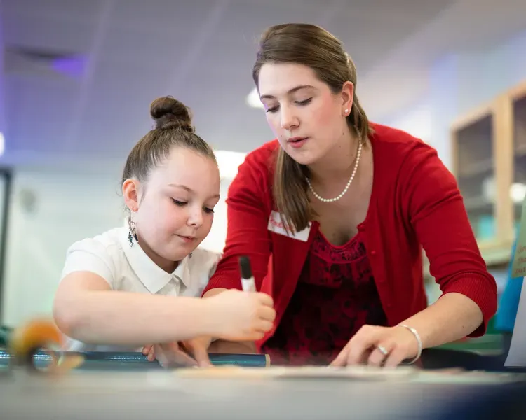 Student teacher with young girl, writing