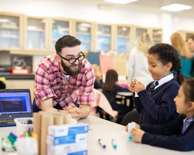 male student with two primary school girls, building something out of cardboard