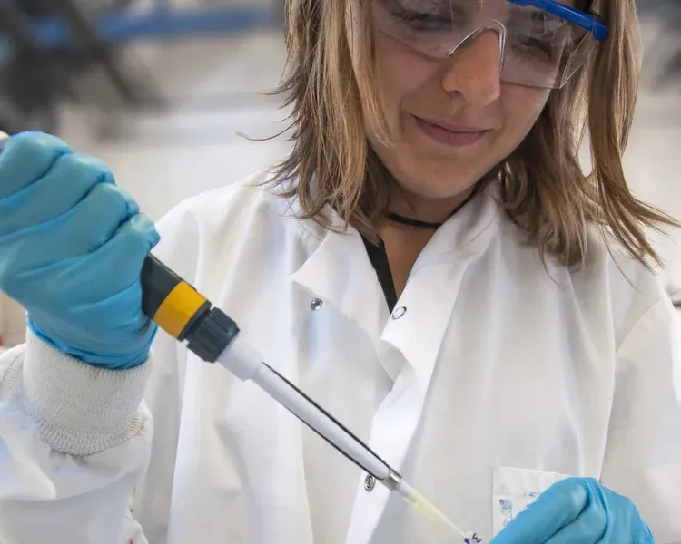 a woman wearing blue gloves and goggles working in a lab testing samples