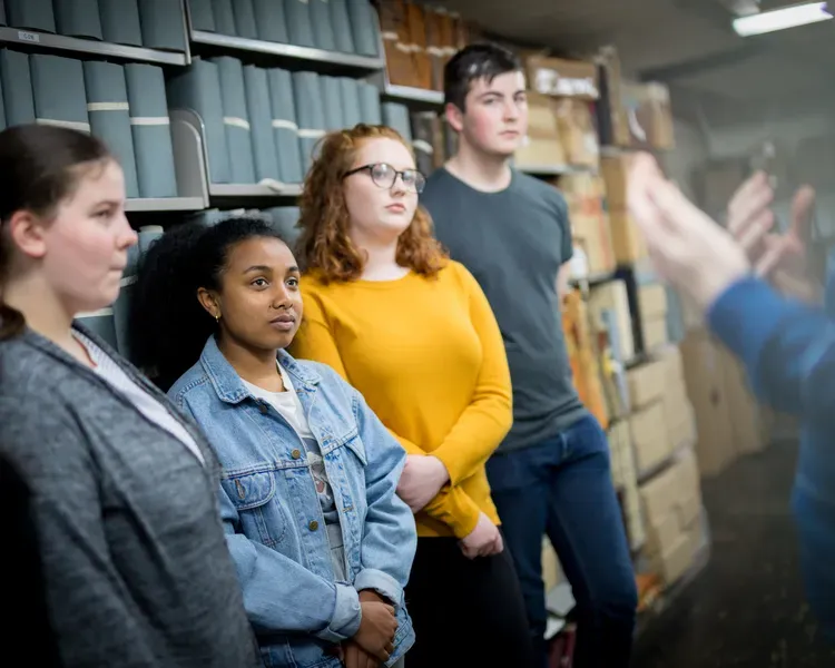 A group of students standing in front of shelves of old books listening to a man speaking