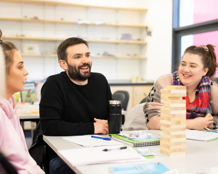students sitting around a desk with a tower made of blocks