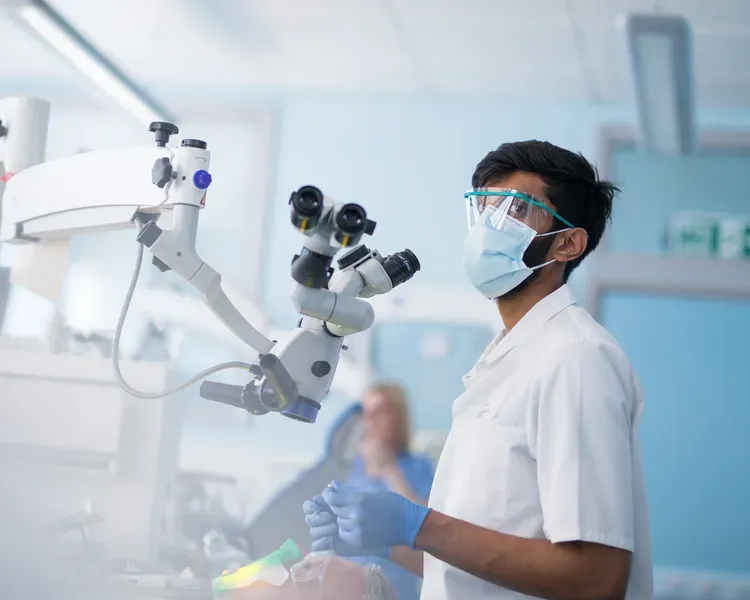 a man wearing a mask and using a microscope to preform dental treatement 