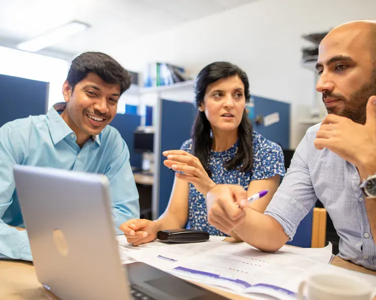 3 people sitting at a desk looking at a laptop