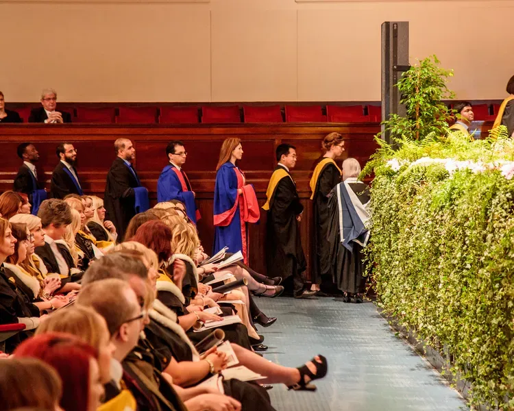The audience is sitting watching the graduation, as graduates line up to collect their certificates