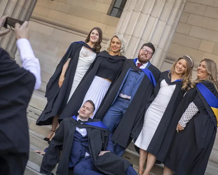 An image of graduates in robes on the stairs of the Caird Hall getting their photo taken