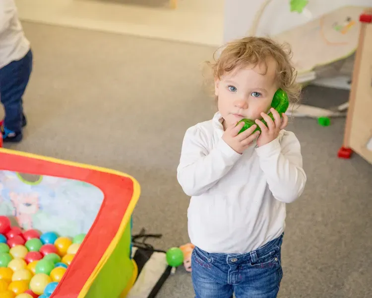 A young girl plays with a toy phone next to a ball pit