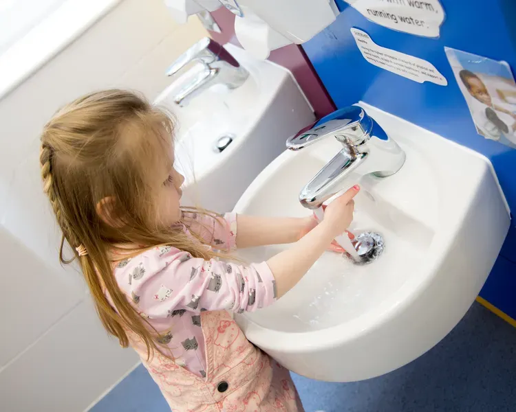 A young girl washes her hands in a sink