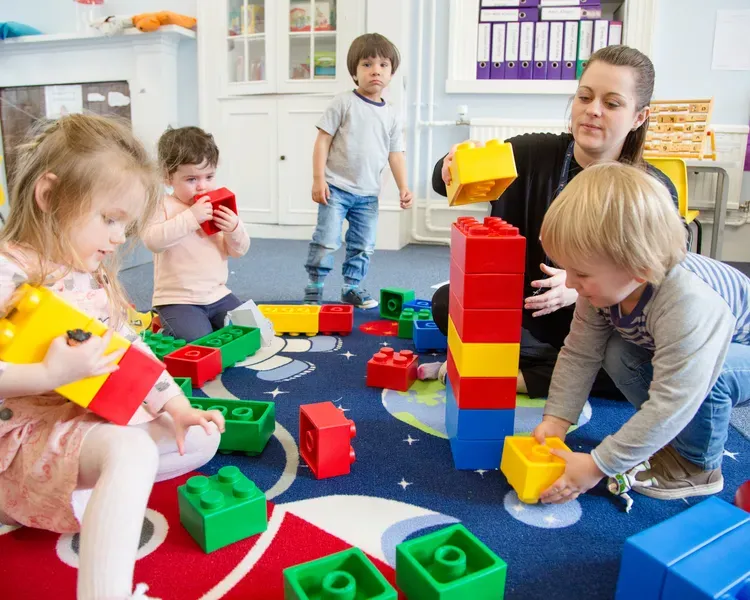 A nursery assistant helps several children build with giant Lego-style blocks
