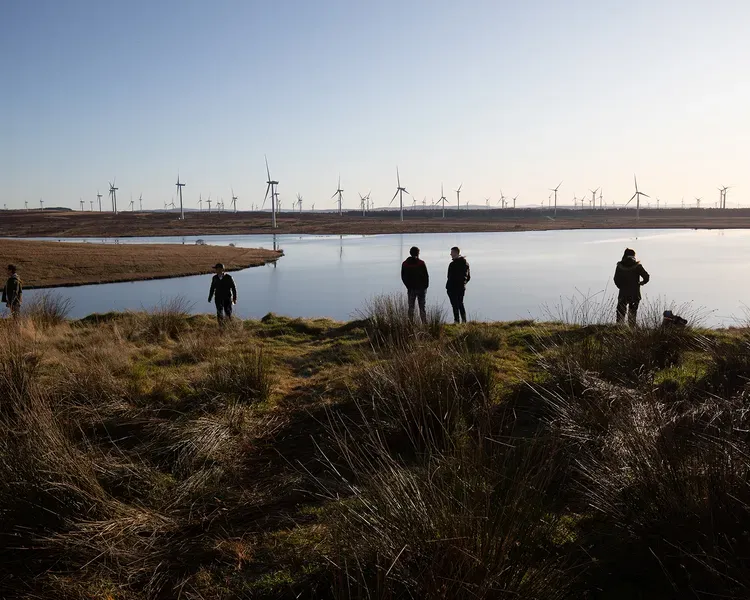 picture of several people looking out across water at a wind farm in the evening