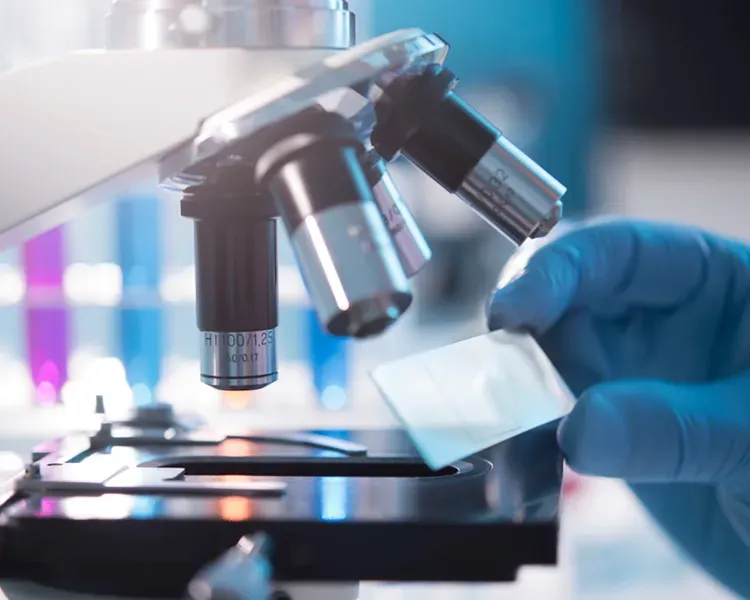 a close shot of a microscope with a gloved hand holding a glass slide