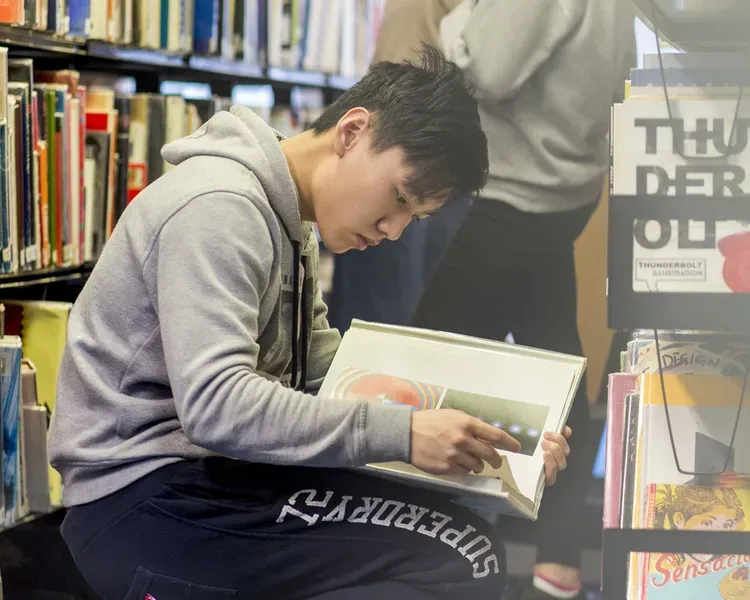 a person sitting in a library between bookshelves reading a book