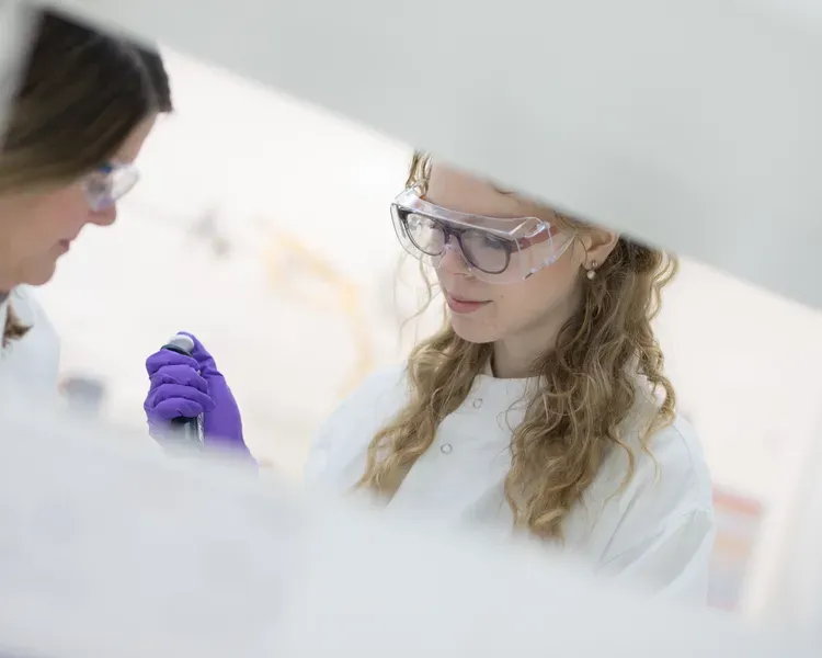 student in a lab holding a test tube, wearing purple gloves and safety glasses