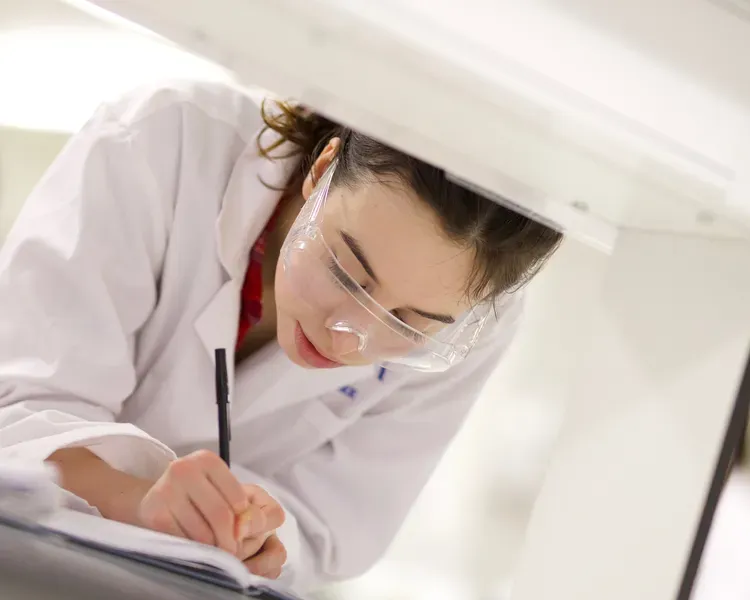 student working in lab in a lab coat, writing with a pen