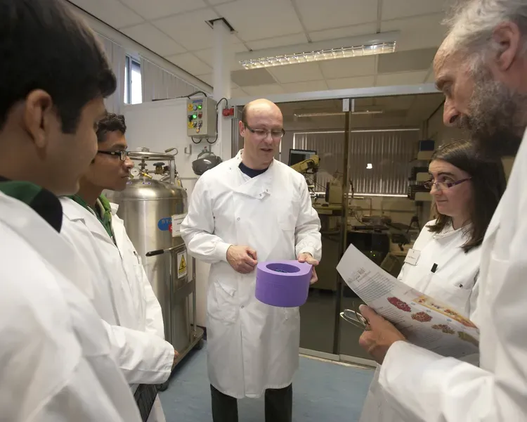 scientists in lab coats, grouped around one who is holding a purple bowl