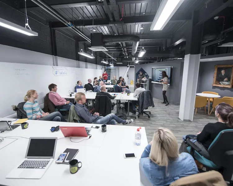 Students listen to a presentation in a room with coworking desks