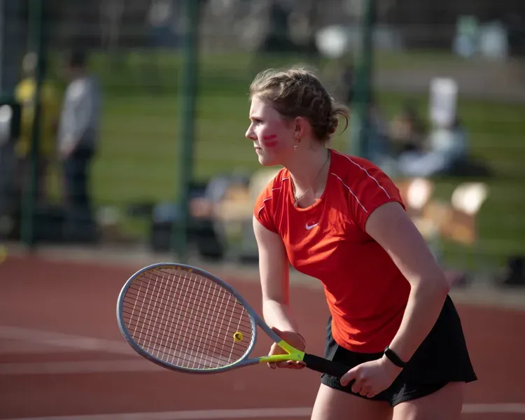 student in red top playing tennis