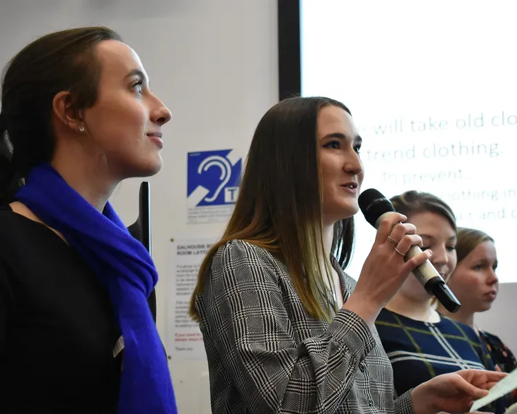 Three people standing side-by-side, the middle person speaking in a microphone and holding a paper