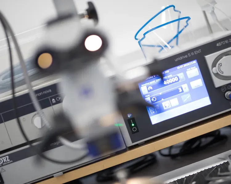 A selection of medical equipment with a small computer screen with cables and and a blurred microscope 