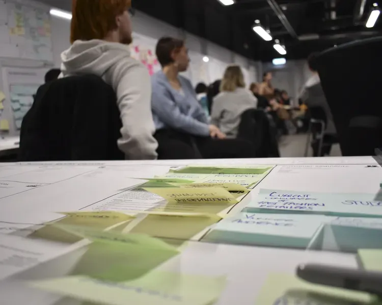 People sitting in a classroom, with post it notes arranged on the table.
