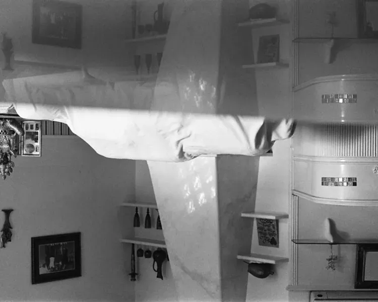Black and white image of the corner of a room, reflected in the middle so the bottom half appears upside down.