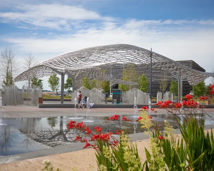 Steel sculpture of whale with fountains and plants in the foreground.