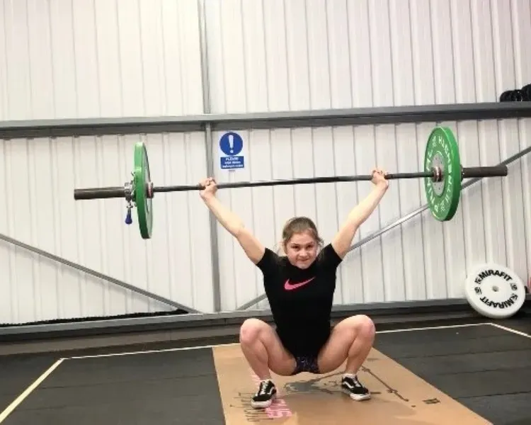 Female weightlifter in squatting position as she lifts a barbell over her head 