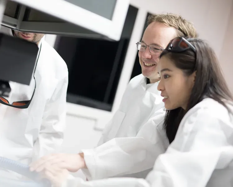 Three people standing over machinery in a lab