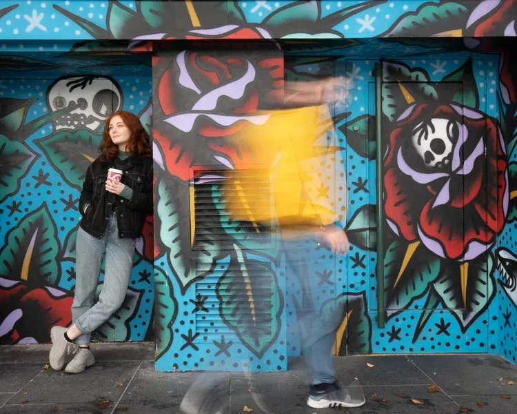 student drinking coffee in front of wall graffiti