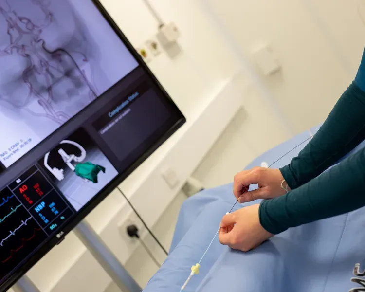 A woman in a hospital room, monitoring her health on a computer screen with medical equipment nearby.
