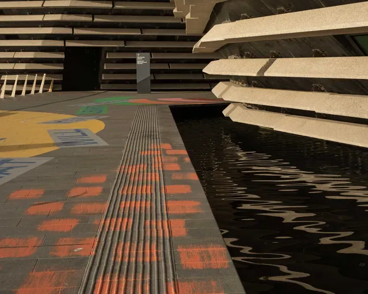 The side of the V&A Dundee building with water below. The pavement has been coloured with bright paints in different patterns.