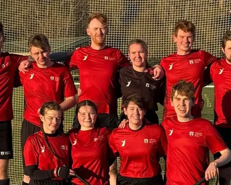A team of shinty players, standing in front of a net wearing red tshirts.