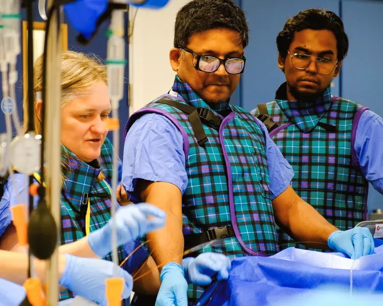 A group of individuals in blue and green uniforms, gathered closely, standing over a table of medical equipment