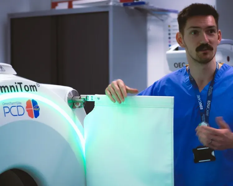 A man in blue scrubs stands with a large machine, indicating a medical or clinical context