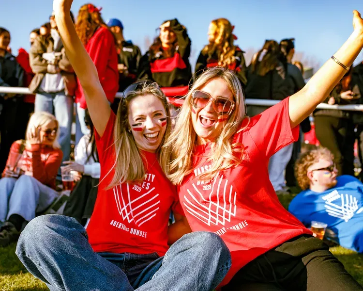 Two people with long hair and red t-shirts smile widely with their arms in the air.