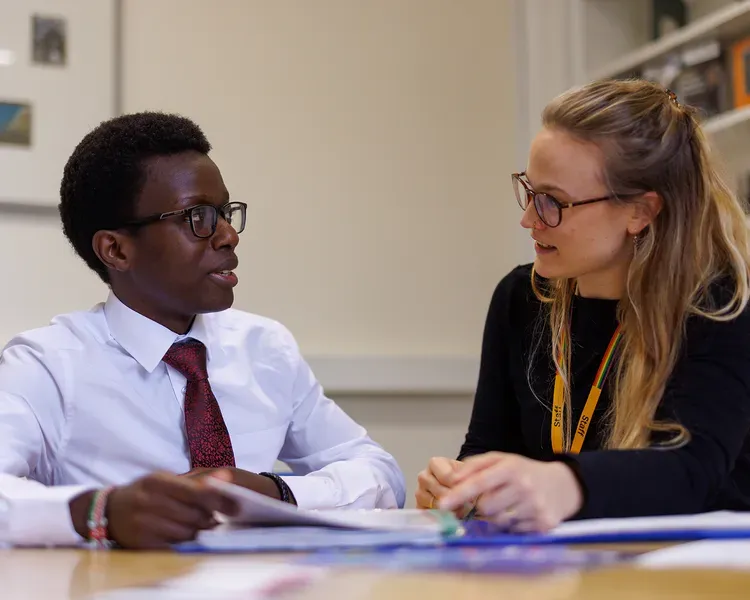 Two people facing each other at a desk with paper work in front of them