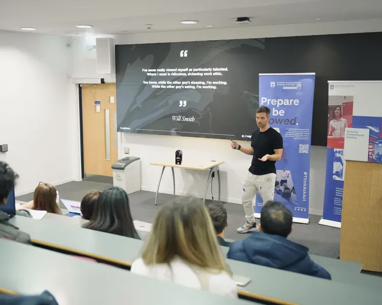 A lecture theatre full of people sitting, looking towards a person at the front who is presenting.