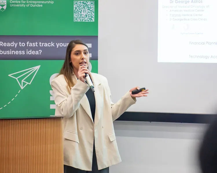 A person standing with a microphone in hand presenting at the Venture 2024 competition