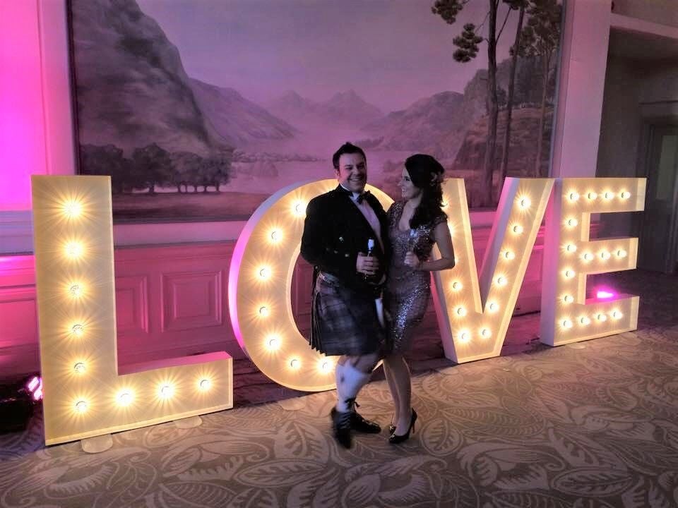 a man and a woman standing in front of a big sign that says Love