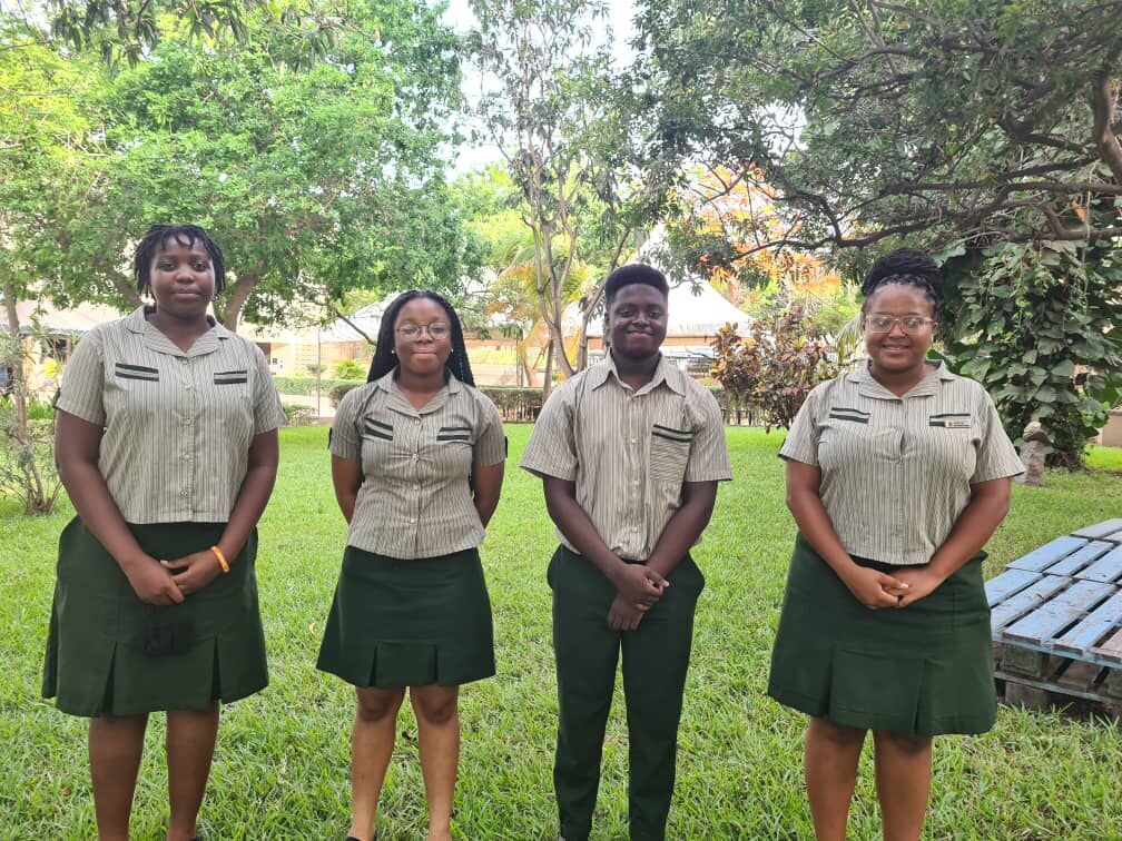 Team members from TIS standing in brown uniform smiling with trees and grass in background