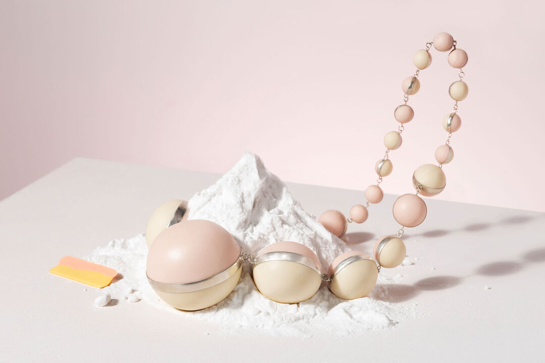 Ceramic necklace of two tone spheres, designed by Rebecca, displayed falling into a small pile of sherbet 