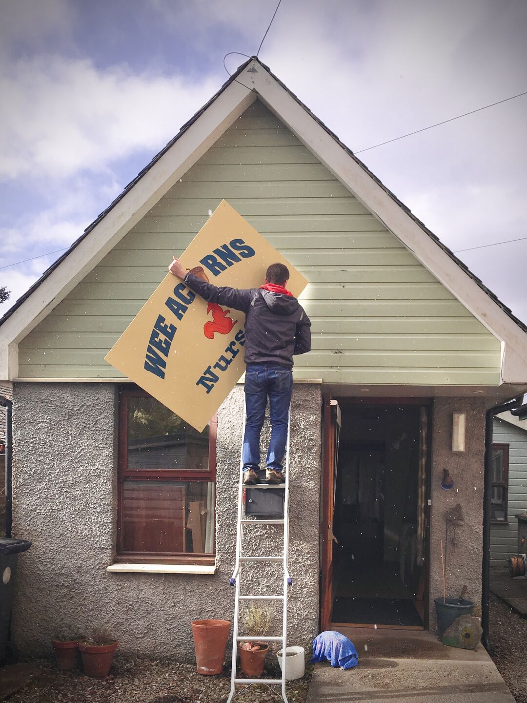 Man on ladder taking down sign on exterior of Central Scotland School of Craft building
