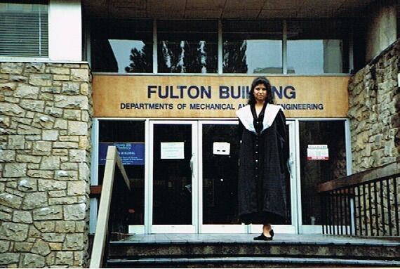 Jay stands outside the Fulton Building in graduation robes