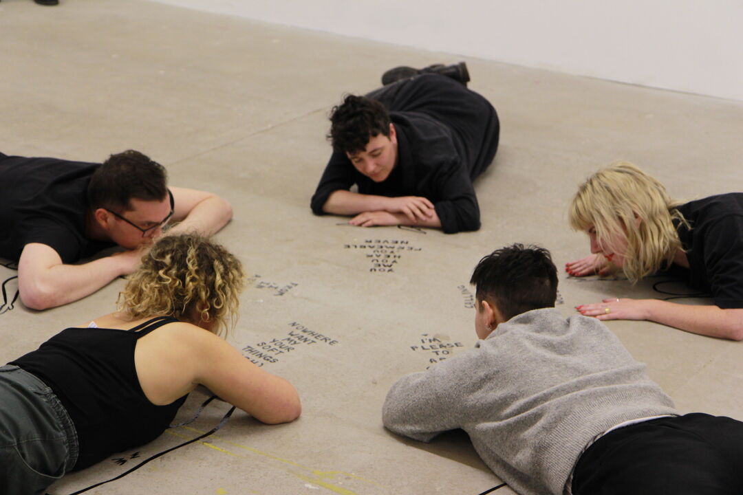 People lying face down on the floor in a circle looking at writing on the floor