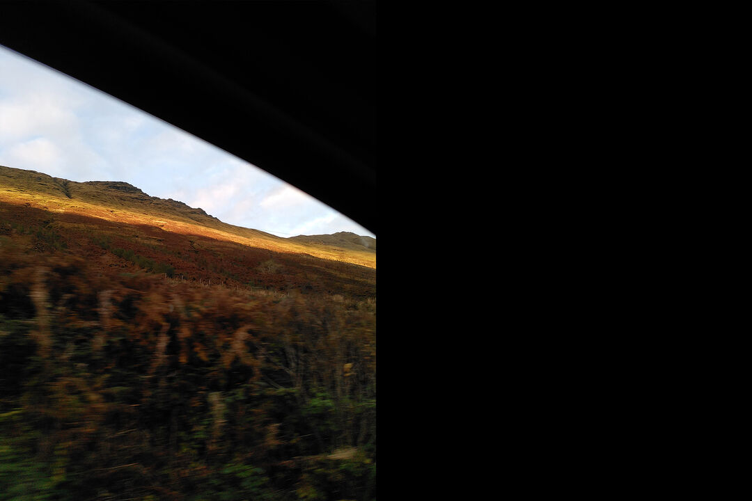 A window frame with a view of a sunlit hill and blue sky