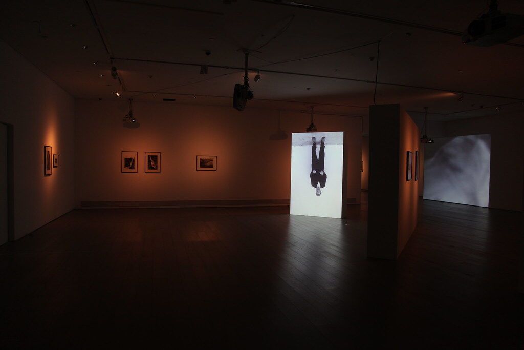 I want my crown exhibition space, smaller photos mounted along the back wall and a large image of a man upside down sits in from the wall at an angle